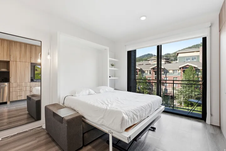 Integrated murphy bed with built-in shelving, large sliding glass doors, private balcony with metal railing, and wood-finish flooring