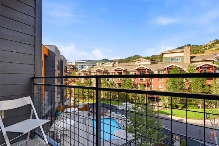 Balcony with metal grid railing, overlooking a swimming pool, paved patio, and surrounding buildings with varied architectural styles