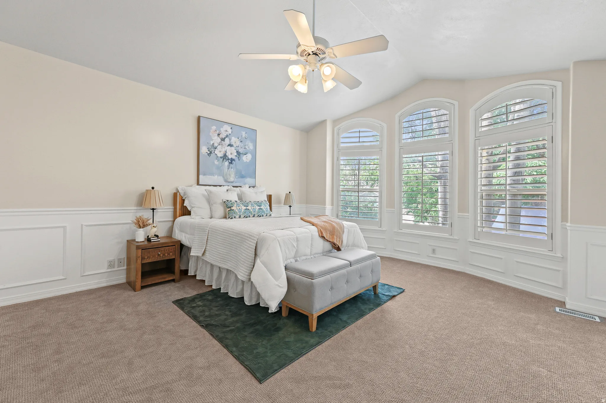 Vaulted ceiling, ceiling fan with integrated lighting, arched windows, plantation shutters, and wainscoting