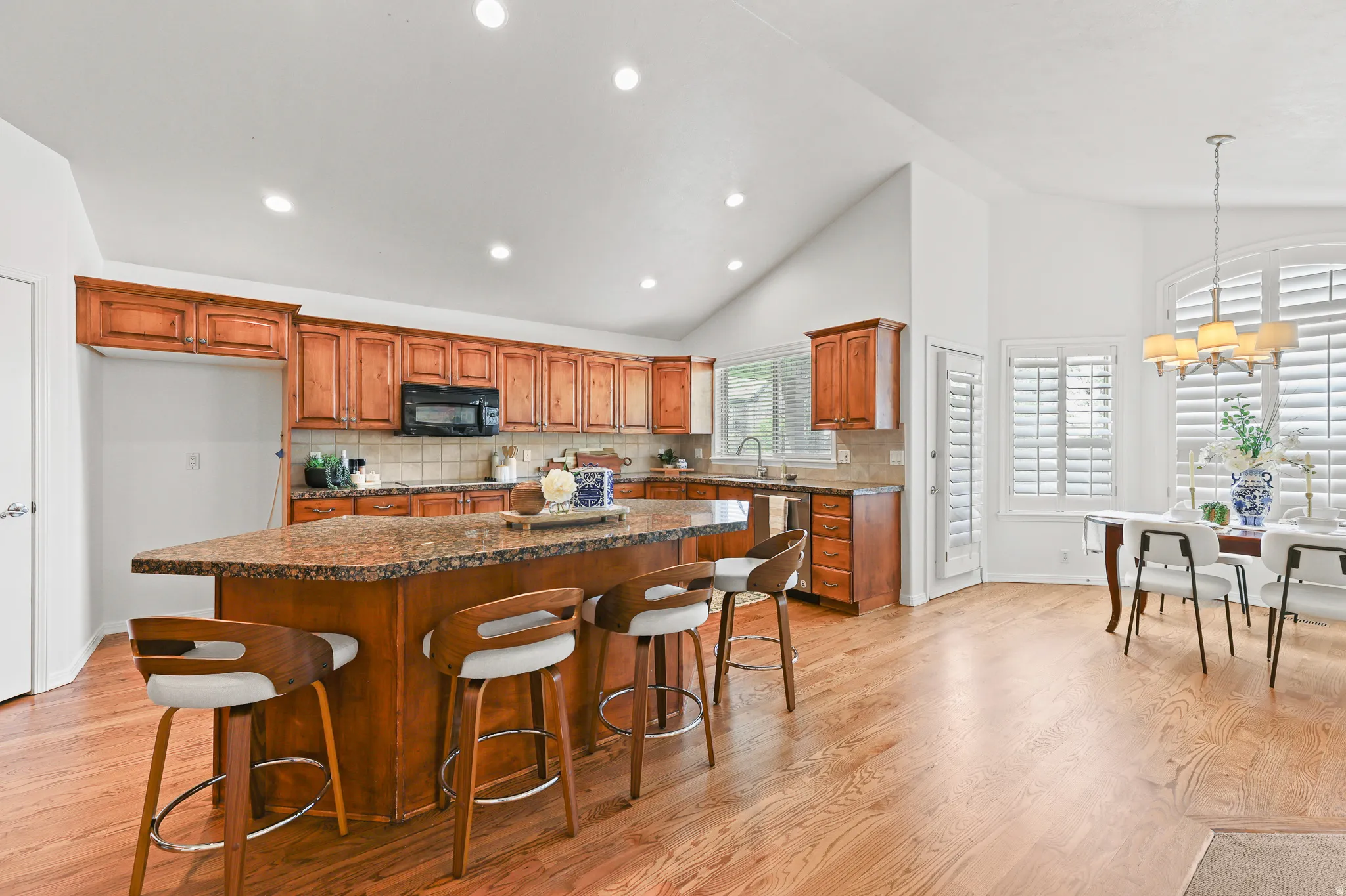 Vaulted ceilings accent the kitchen and dining areas, featuring wood-finish flooring, recessed lighting, and a kitchen island with seating