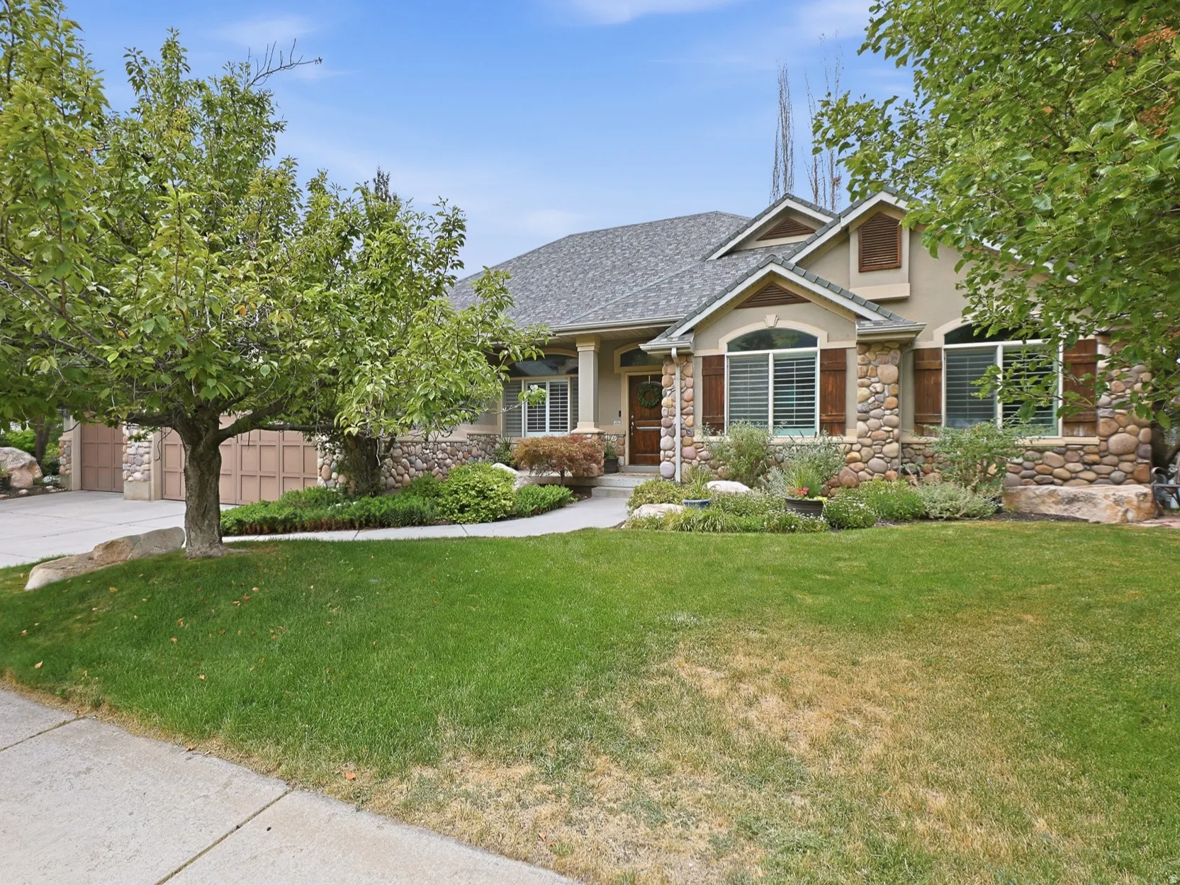 Stone and stucco exterior with decorative shutters, a covered entry, an attached garage, and a concrete driveway