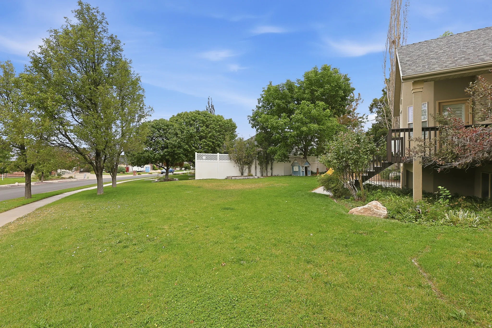 Expansive grassy yard with mature trees, a private deck, and a white fence