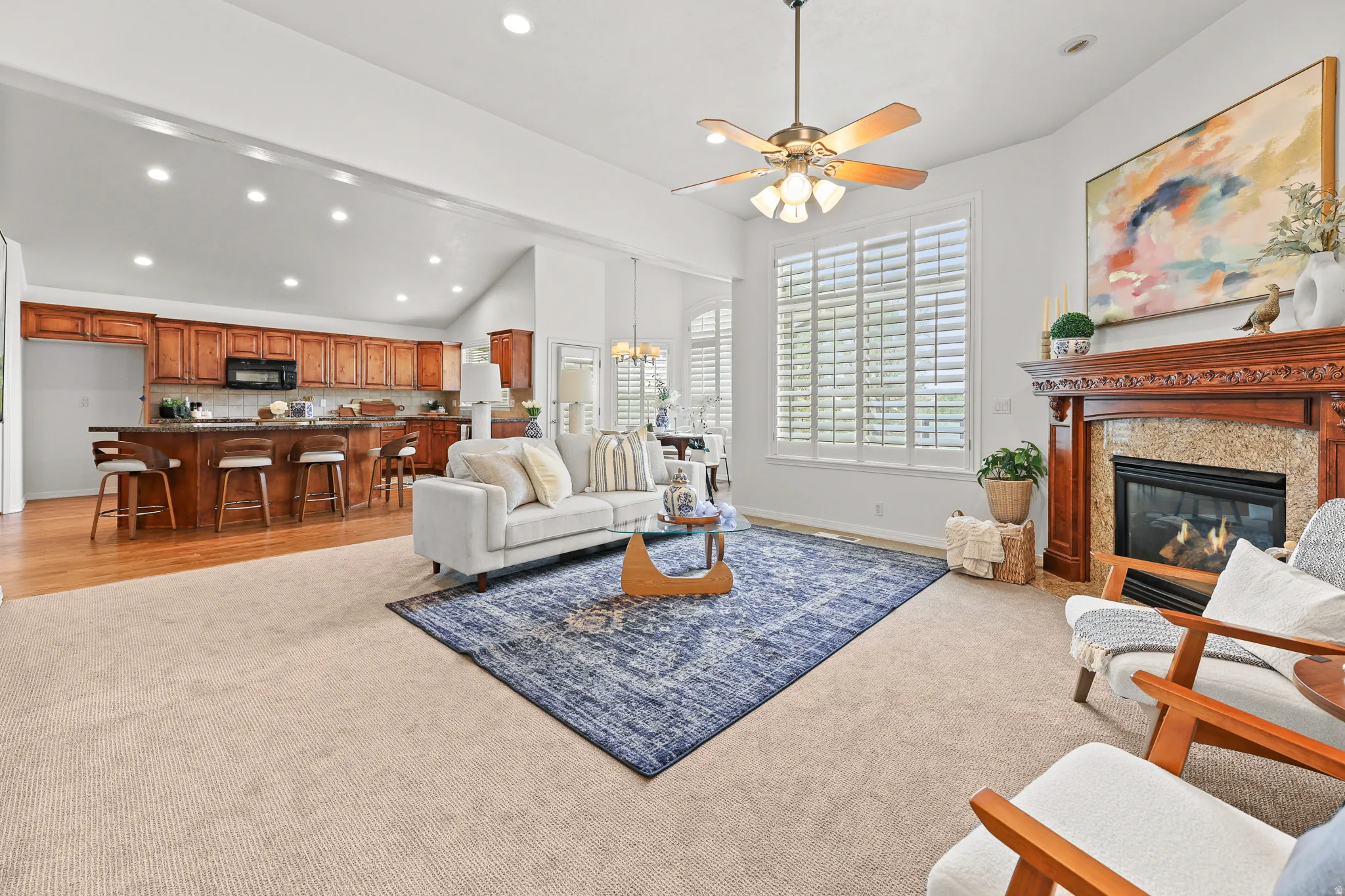 Spacious living area featuring a fireplace with a carved wood mantel, a ceiling fan with integrated lighting, and plantation shutters