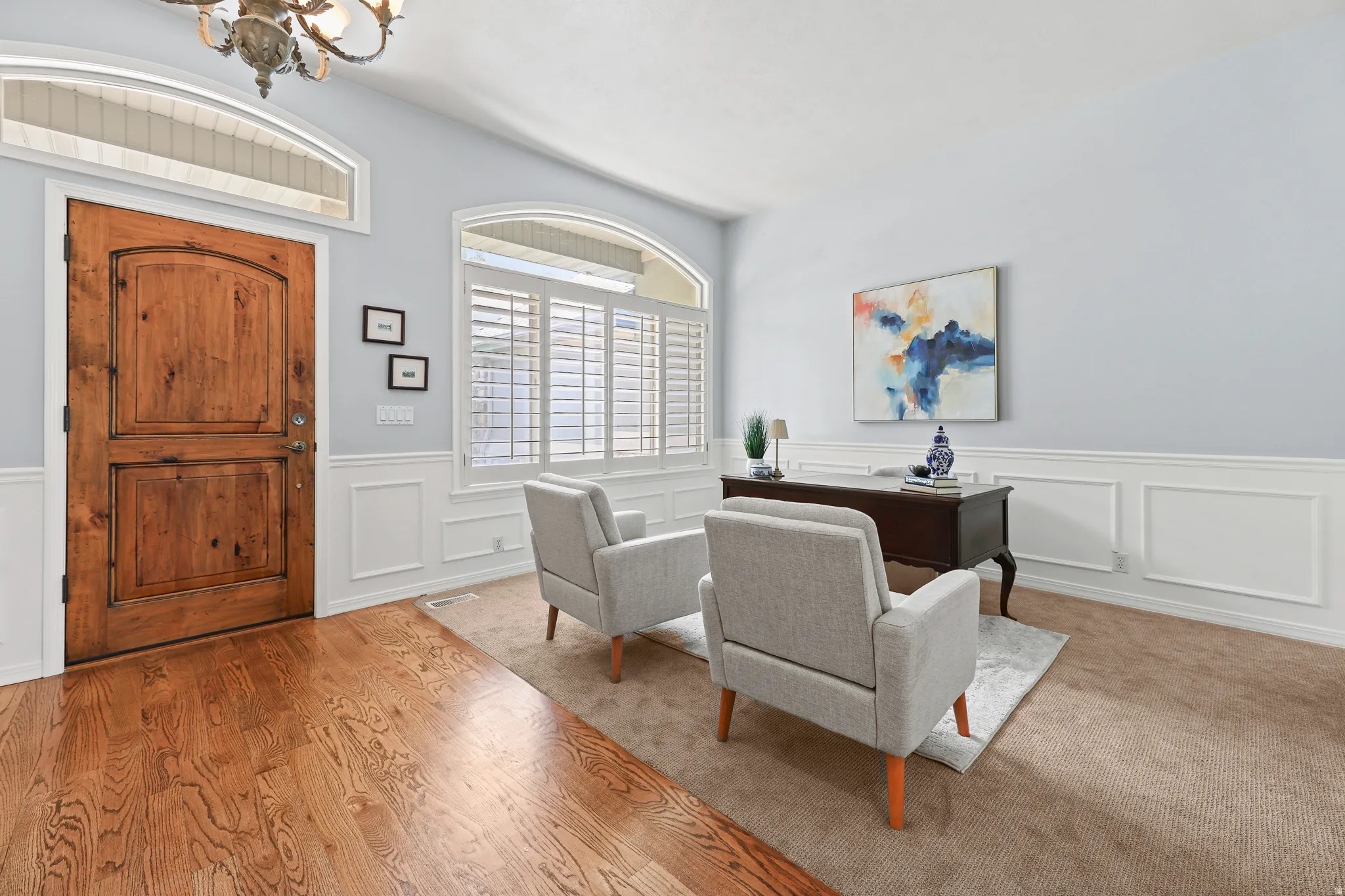 Arched entry door with wood finish, arched transom window, wood-finish flooring, and white wainscoting