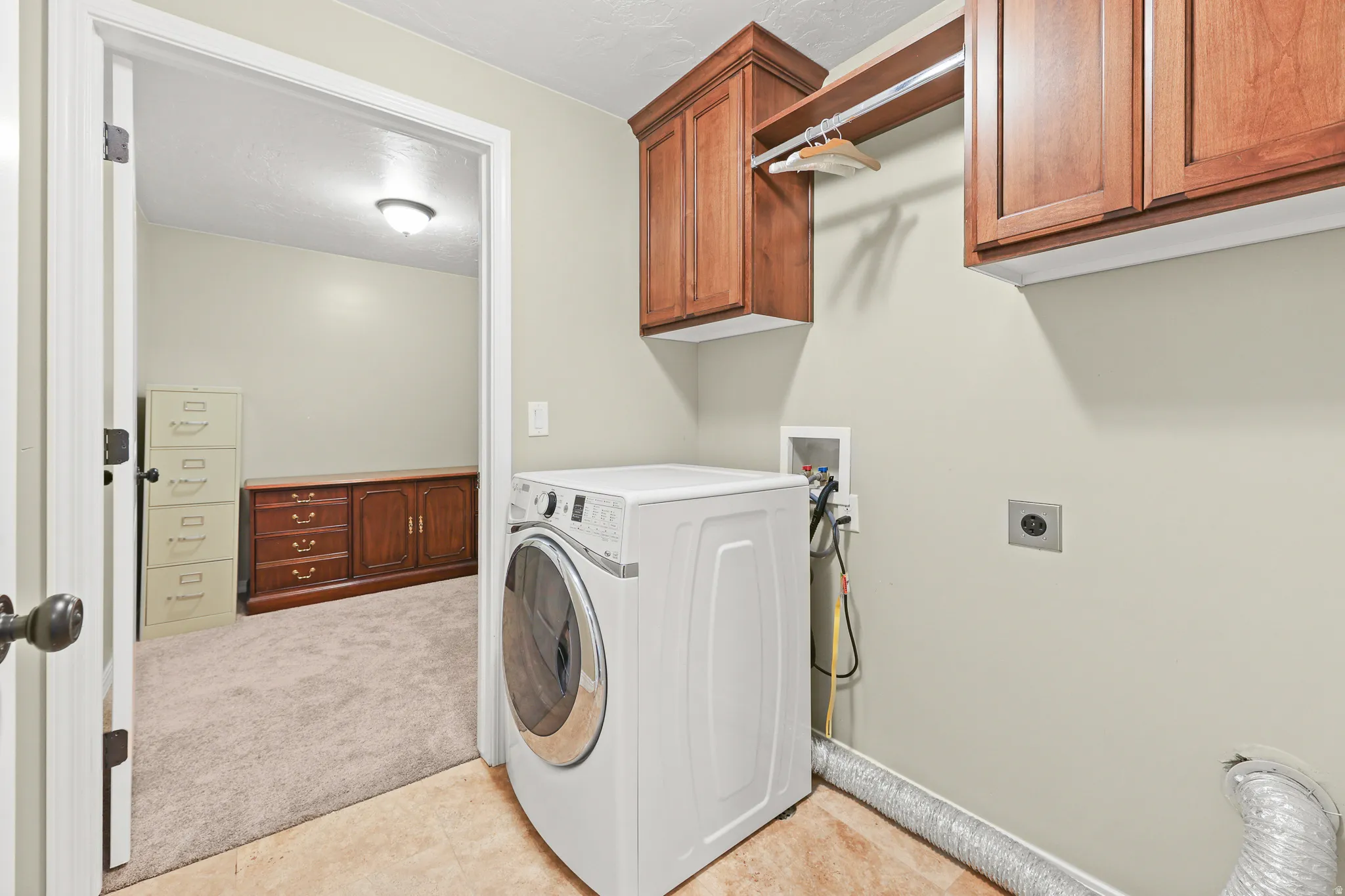 Laundry area featuring wood cabinetry, integrated hanging rod, and tile flooring