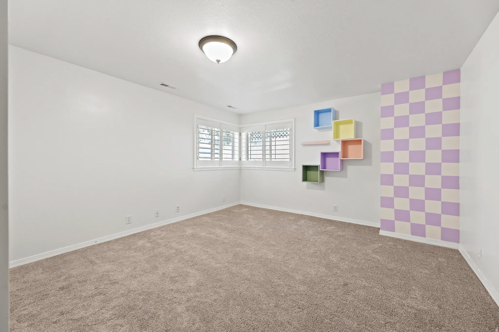 Soft pile carpet flooring, white painted walls, window with plantation shutters, ceiling-mounted light fixture, decorative wall shelving
