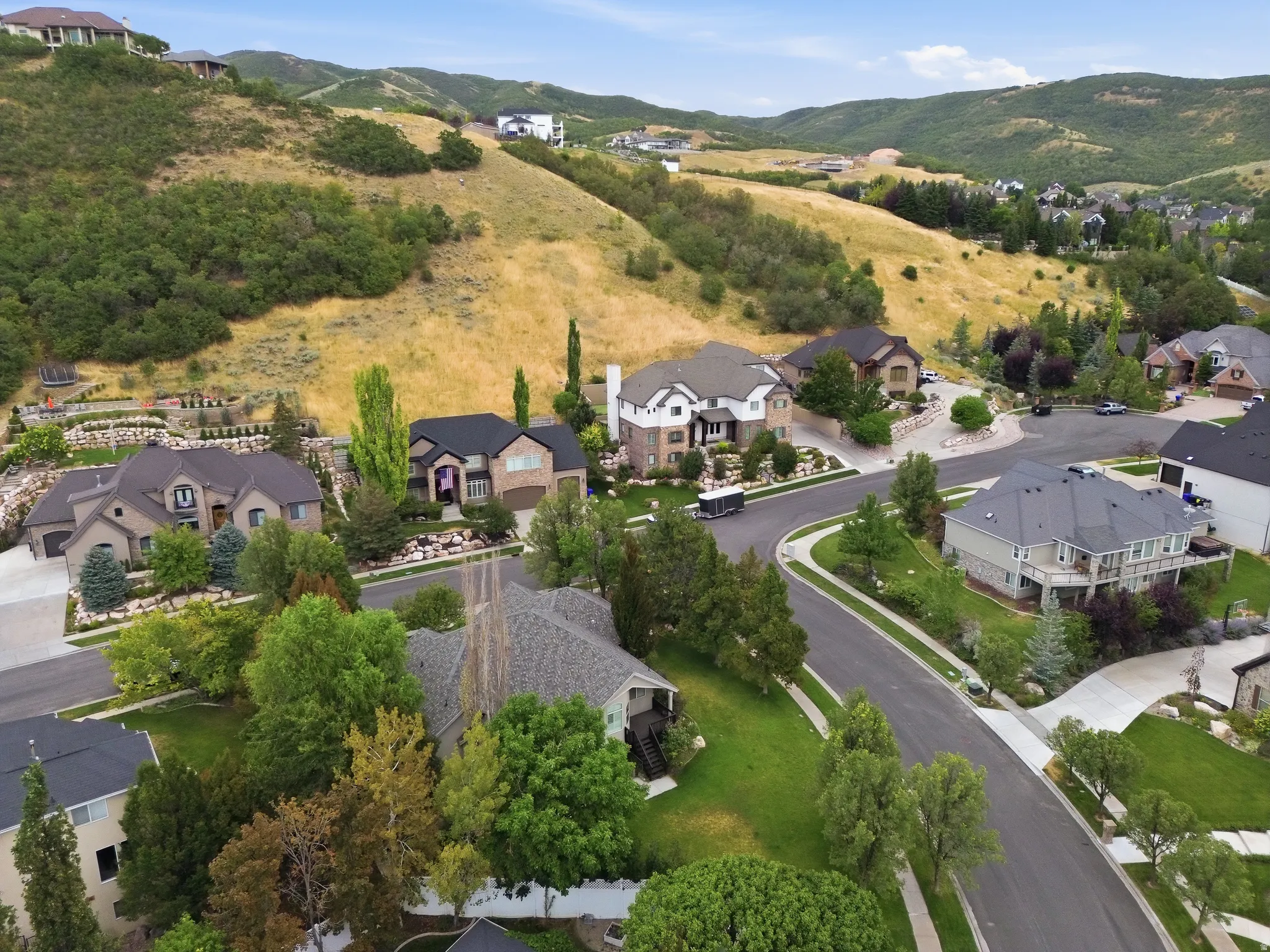 Residential neighborhood with landscaped properties, paved roadways, mature trees, and mountainous terrain