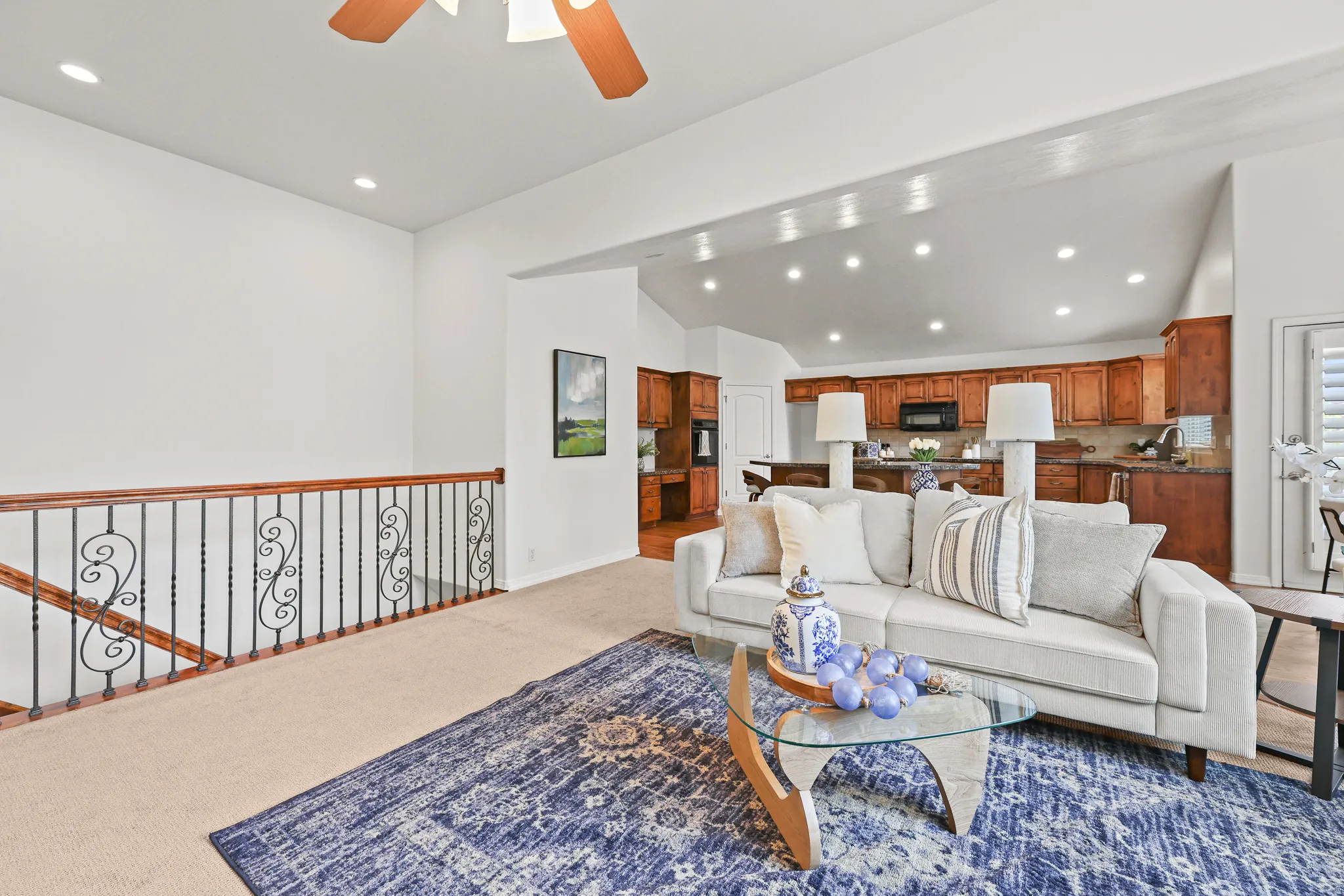Open-concept living space with vaulted ceilings, recessed lighting, and a wood-finish railing with decorative metal spindles