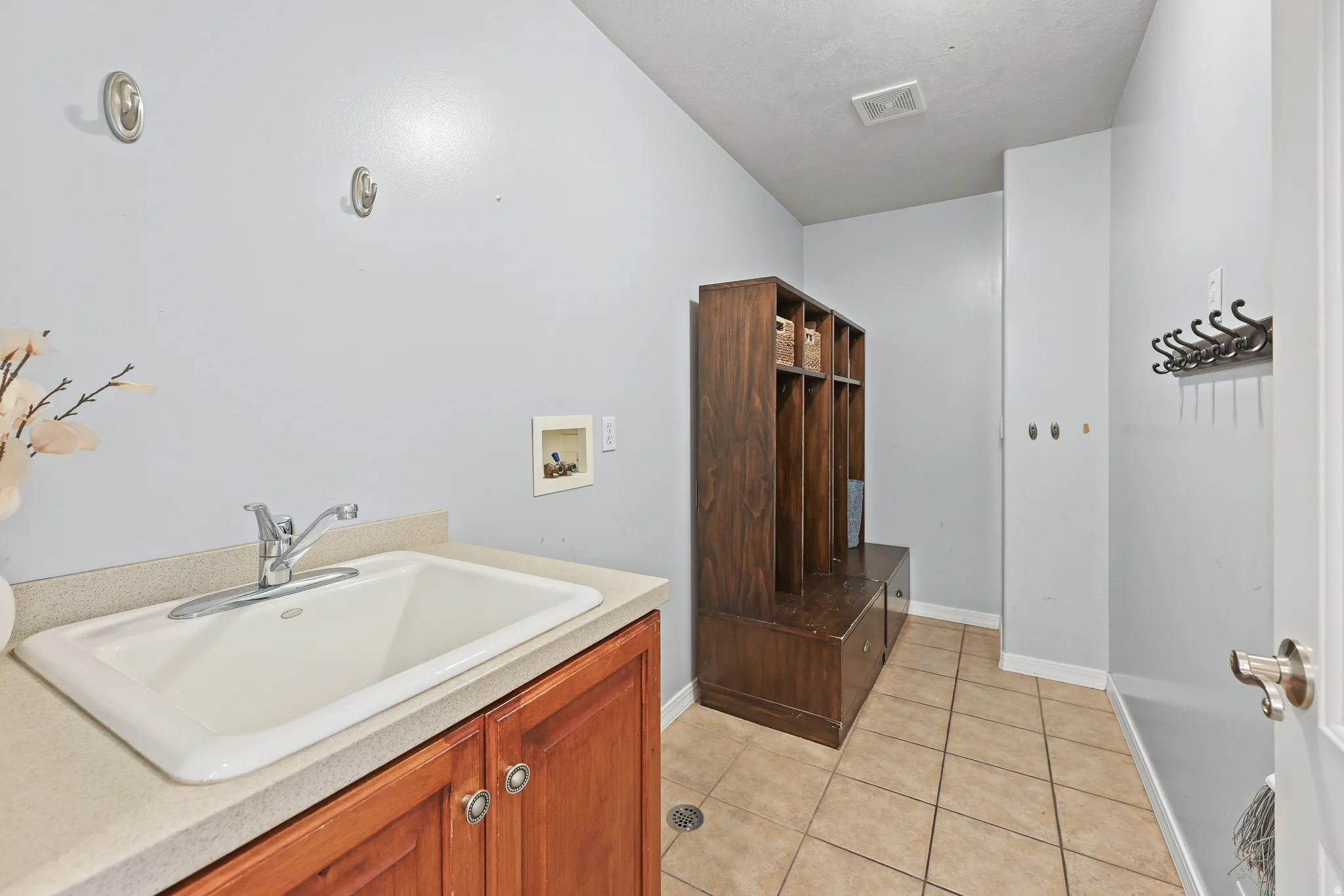 Utility sink with countertop, wood-finish cabinetry, and tile flooring