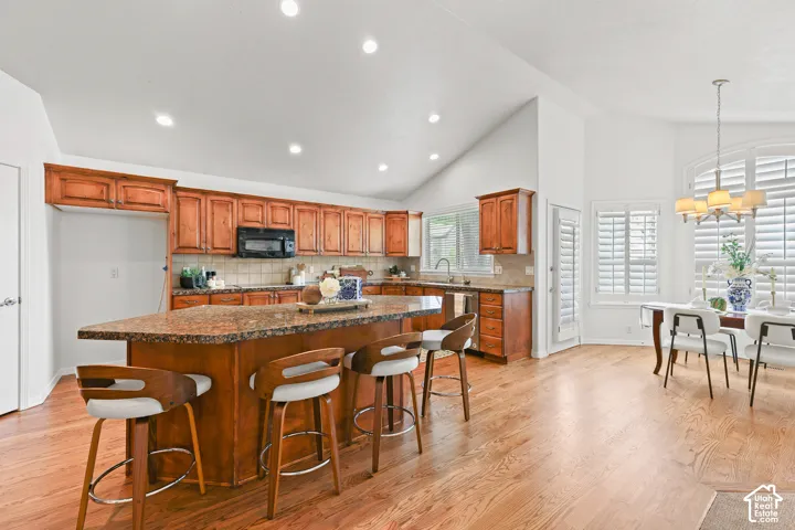 Vaulted ceilings accent the kitchen and dining areas, featuring wood-finish flooring, recessed lighting, and a kitchen island with seating