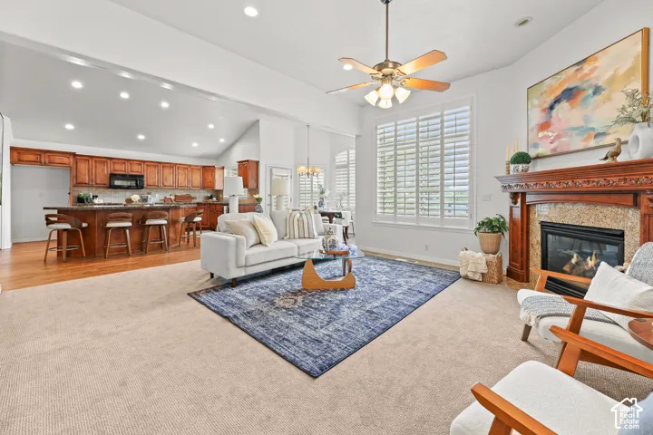 Spacious living area featuring a fireplace with a carved wood mantel, a ceiling fan with integrated lighting, and plantation shutters