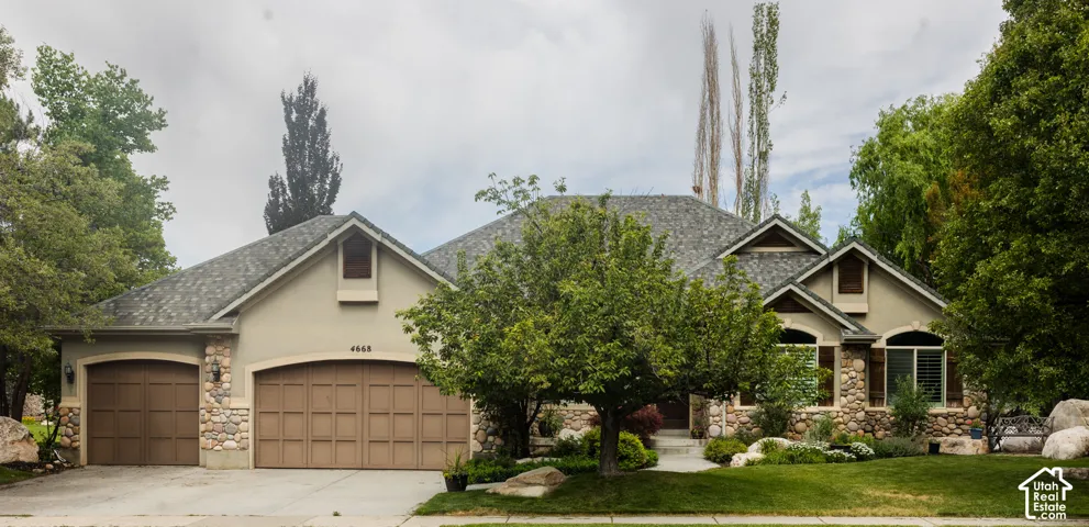 Stucco exterior with stone accents, featuring a multi-car garage, arched garage door openings, and mature landscaping