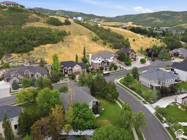 Residential neighborhood with landscaped properties, paved roadways, mature trees, and mountainous terrain