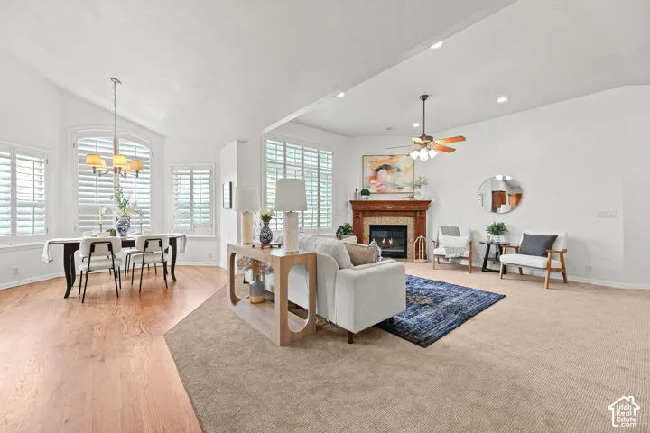 Vaulted ceilings, wood-finish flooring, plantation shutters, gas fireplace with a decorative mantel, and a ceiling fan with integrated lighting