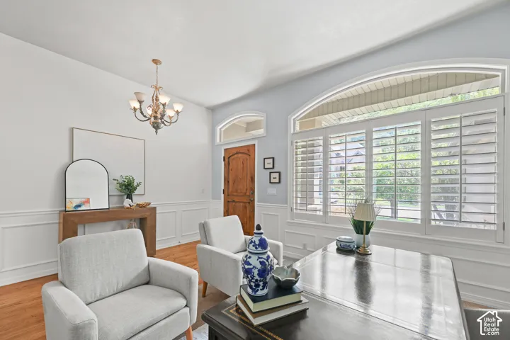 Arched window with plantation shutters, wood-finish flooring, wainscoting, wood panel door, and an ornate chandelier