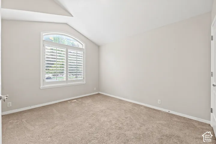 Arched window with plantation shutters, vaulted ceiling, neutral wall color, and wall-to-wall carpeting