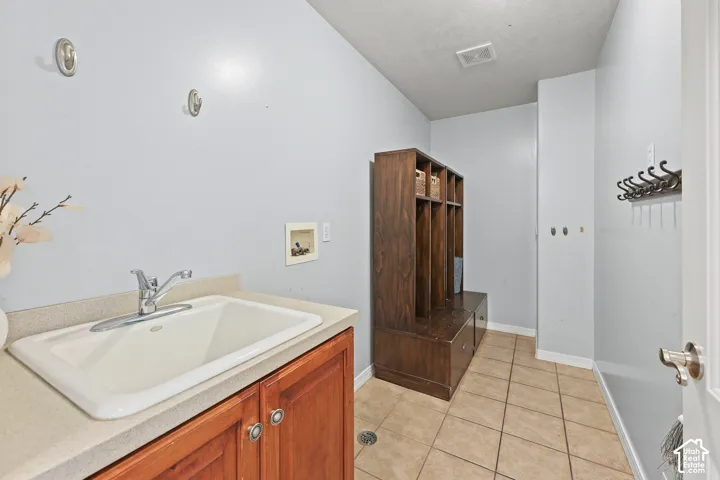 Utility sink with countertop, wood-finish cabinetry, and tile flooring