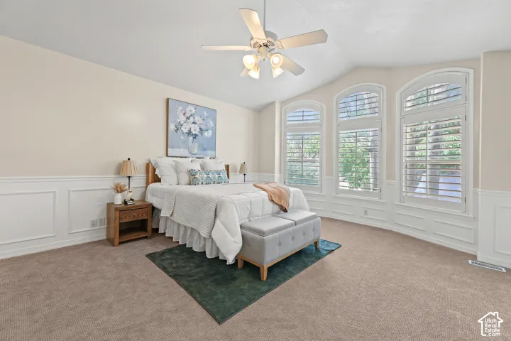 Vaulted ceiling, ceiling fan with integrated lighting, arched windows, plantation shutters, and wainscoting