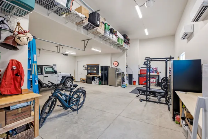 Spacious garage featuring polished concrete flooring, overhead storage shelving, built-in cabinetry, and ample natural lighting from skylights and recessed fixtures