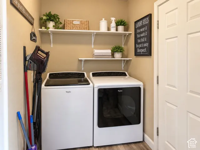 Dedicated laundry room featuring side-by-side Whirlpool washer and dryer with black accents, open shelving with decorative storage containers, and organized utility storage on the wall