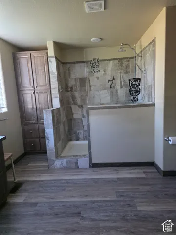 Walk-in shower with tiled surround, wood-finish flooring, and built-in cabinetry
