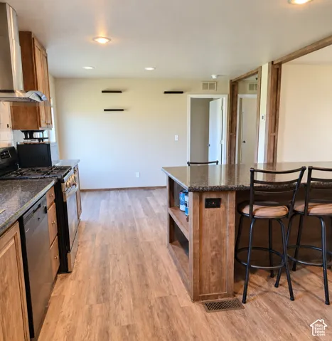Kitchen featuring wood-finish flooring, recessed lighting, wood cabinetry, and a center island with a stone-finish countertop