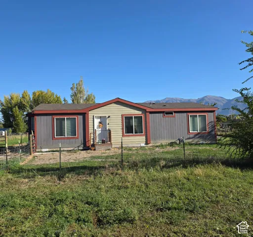 Single-story residence featuring a partial porch with railing, multiple windows, and a mountain backdrop
