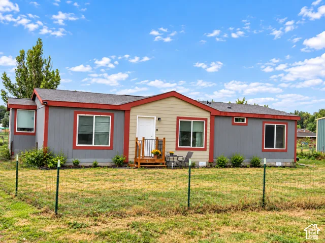 Manufactured home featuring gray and tan siding with red trim accents, a front entry deck, and a fenced yard
