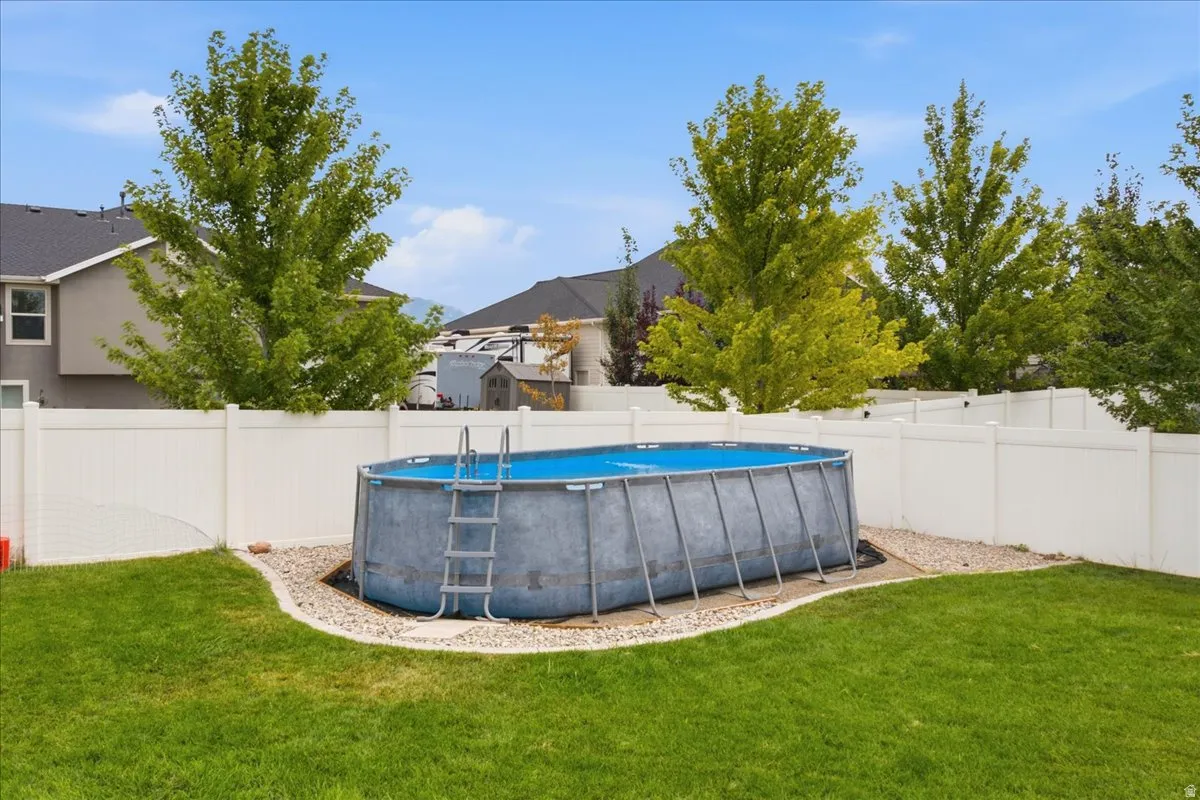 Expansive green lawn featuring a white privacy fence, mature trees, and an above-ground swimming pool with an attached ladder
