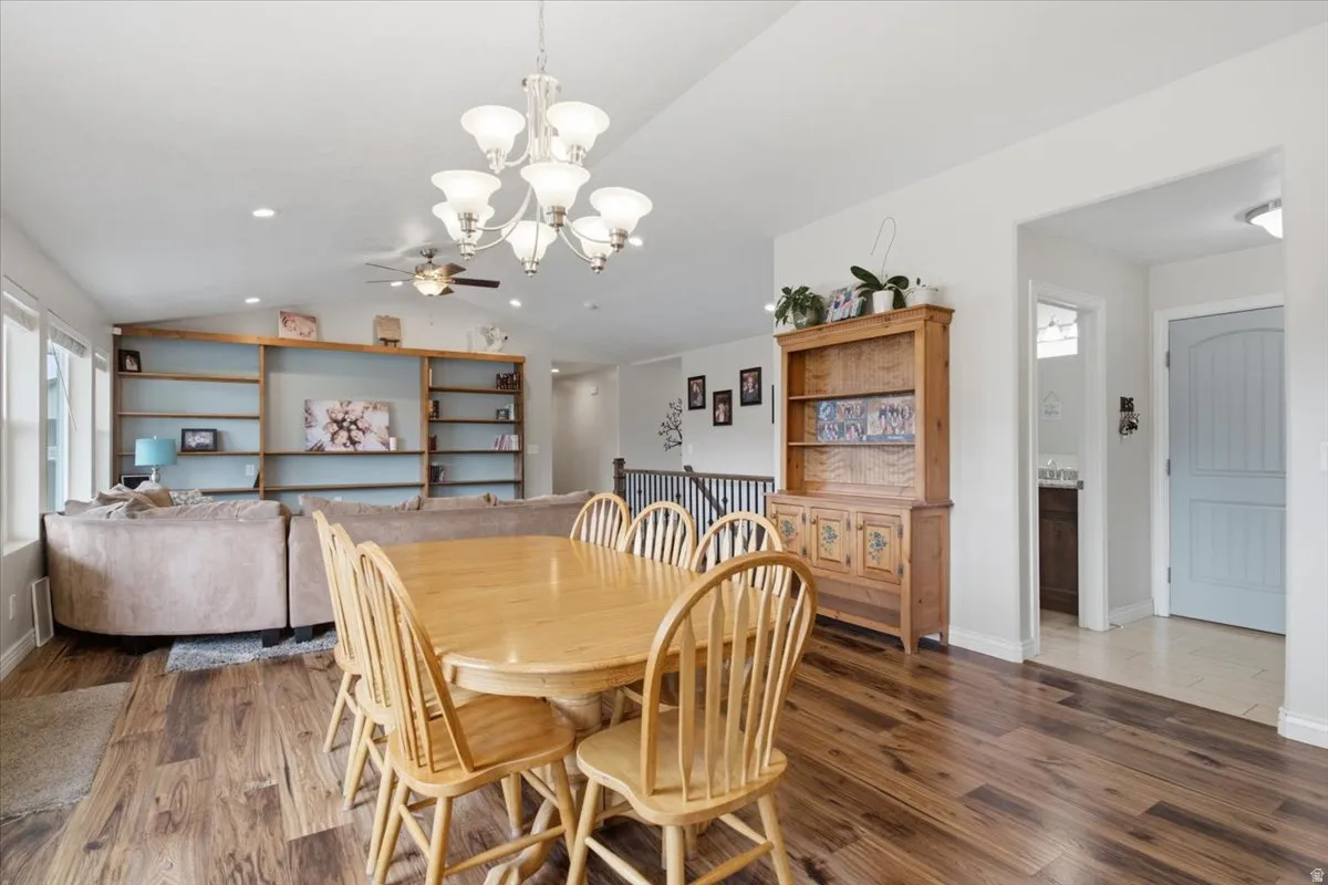Open-concept dining and living area featuring hardwood flooring throughout, a wood dining table with seating for six, and a generous layout illuminated by a multi-arm pendant fixture