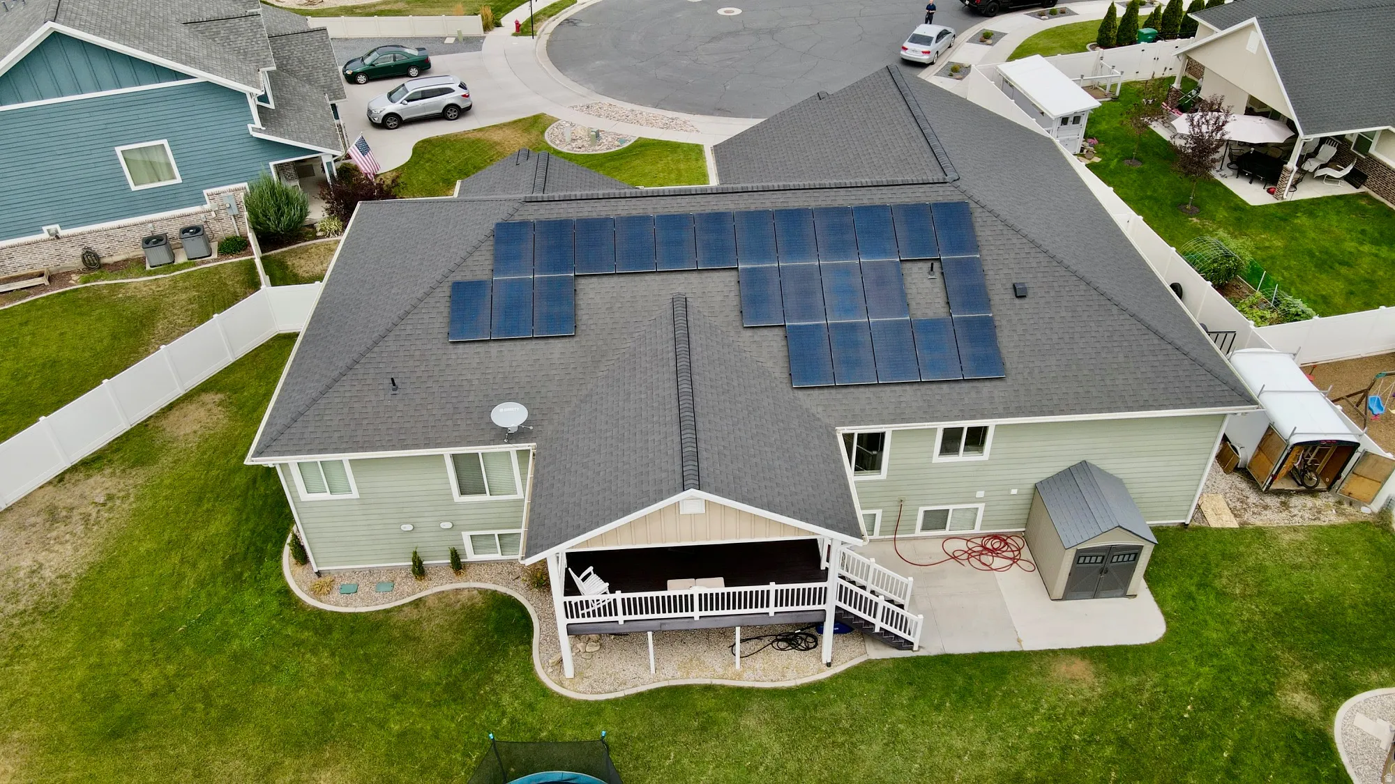 Modern home featuring a spacious rear deck with white railings, manicured lawn, and solar panel array on the roof