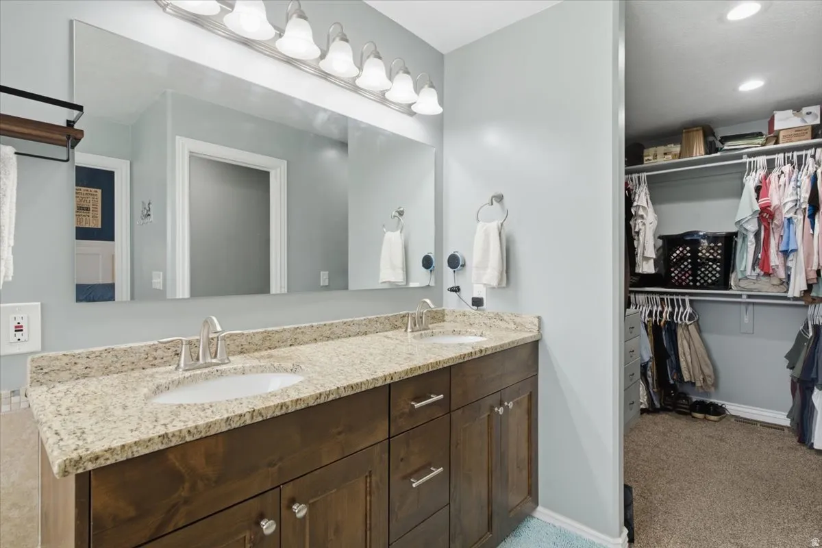 Spa-inspired primary bathroom vanity featuring dual sinks, extensive quartz countertop with undermount basins, warm wood cabinetry with ample storage, polished nickel hardware, and a large illuminated mirror