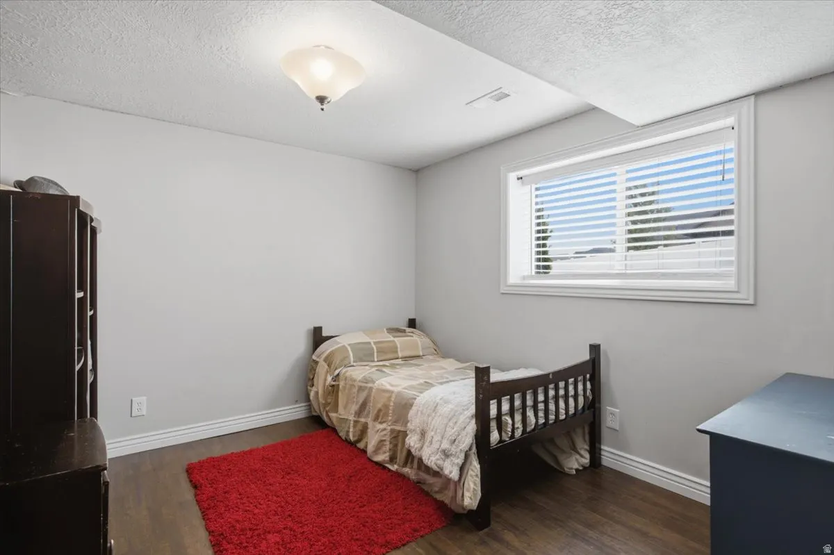 Bright secondary bedroom featuring wood-finish flooring, a large double-hung window with plantation shutters providing natural light, and ample wall space for furnishings