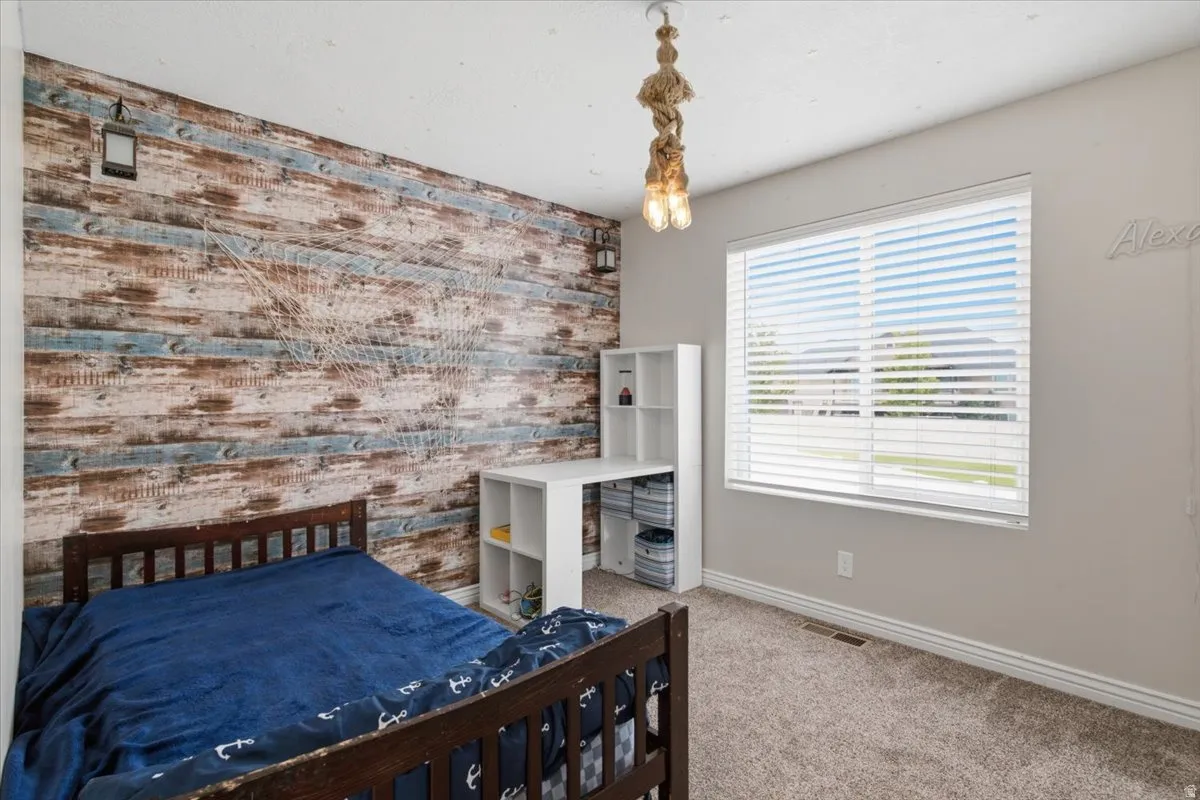 Accent wall with wood-finish paneling, overhead lighting fixture, large window with blinds, and carpeted flooring