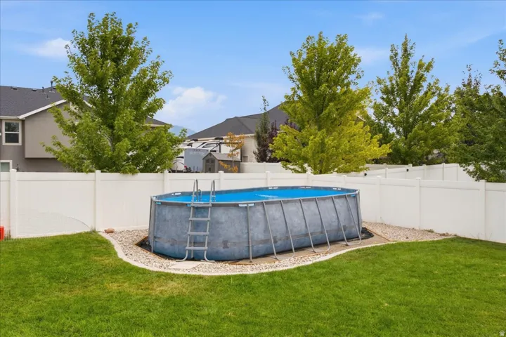 Expansive green lawn featuring a white privacy fence, mature trees, and an above-ground swimming pool with an attached ladder