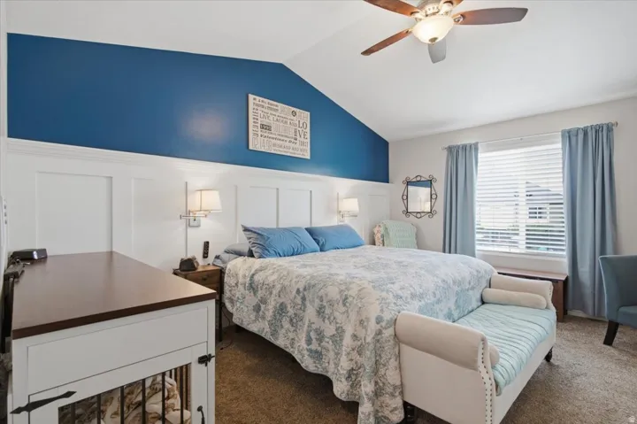 Master bedroom featuring a blue accent wall with white wainscoting, ceiling fan with integrated lighting, wood-finish flooring, and large windows with blue drapery