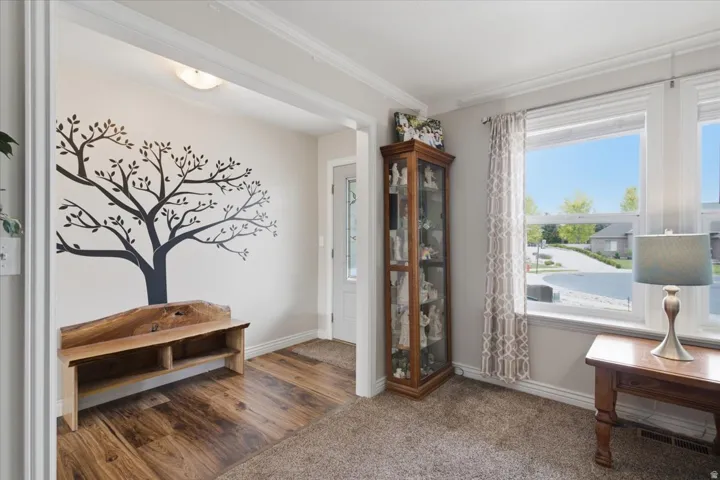 Bright corner den featuring hardwood flooring, large dual windows with natural light, decorative tree wall decal, built-in wooden bench with open shelving, tall glass display cabinet, and pendant lighting fixture