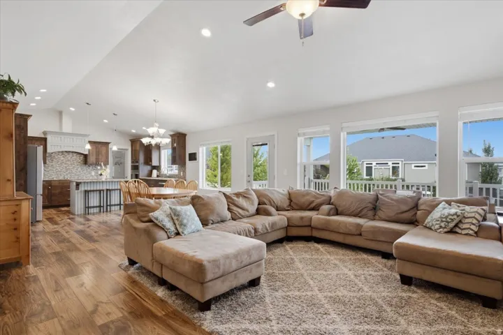 Open-concept living space featuring a substantial sectional layout anchored by wood-finish flooring, a neutral area rug, and abundant natural light from multiple large windows and glass doors