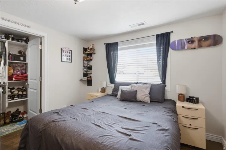 Comfortable bedroom featuring a wood-finish flooring, ample natural light from a large window with custom drapery, built-in shelving along the wall, and a wood-finish nightstand
