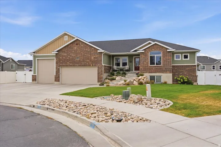 Brick ranch home featuring a two-car attached garage, professionally landscaped front yard with decorative stone beds and mature lawn, and a covered entry with stone detailing