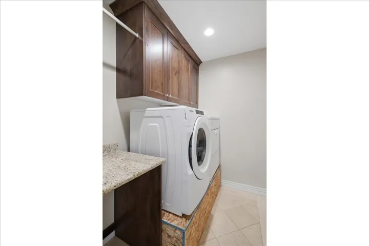 Dedicated laundry room featuring custom wood cabinetry with granite countertop workspace, tile flooring, recessed lighting, and room for full-size front-load washer and dryer appliances