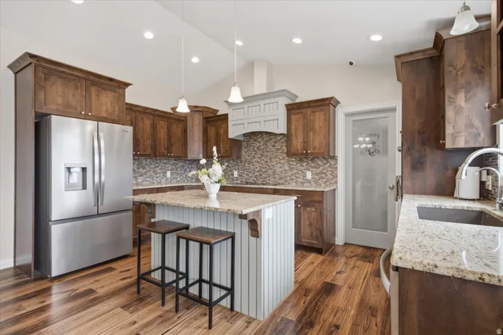 Gourmet kitchen featuring rich wood cabinetry, stainless steel French-door refrigerator, mosaic tile backsplash, granite countertops, and a white island with seating