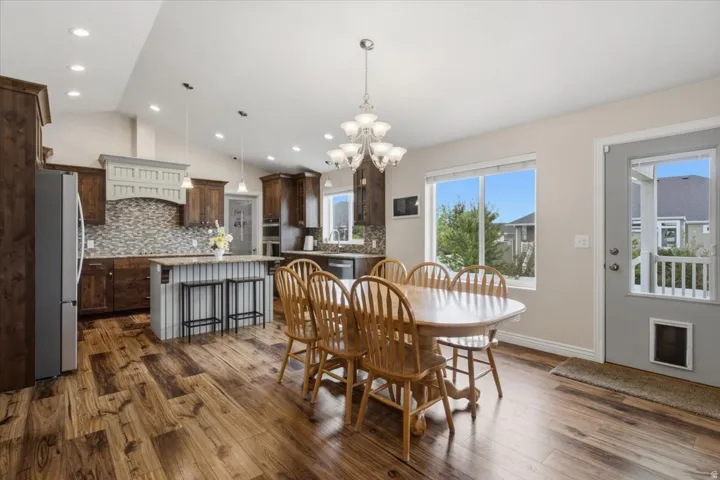 Vaulted ceiling with recessed lighting, wood-finish flooring, full kitchen with stainless steel appliances, central island with seating, and a glass-paneled door