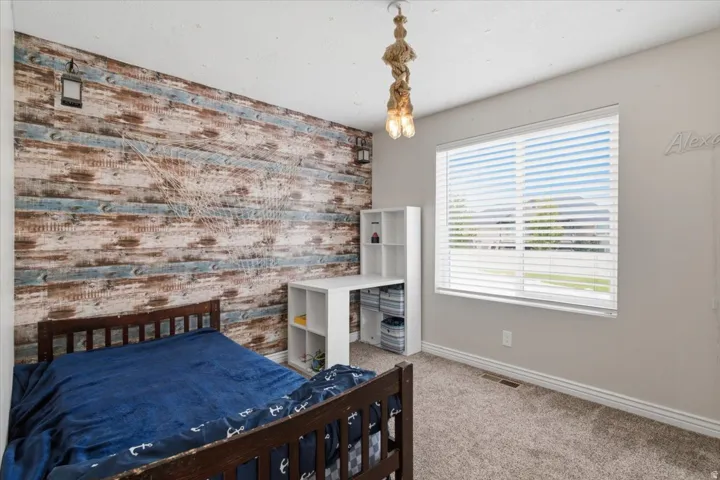 Accent wall with wood-finish paneling, overhead lighting fixture, large window with blinds, and carpeted flooring