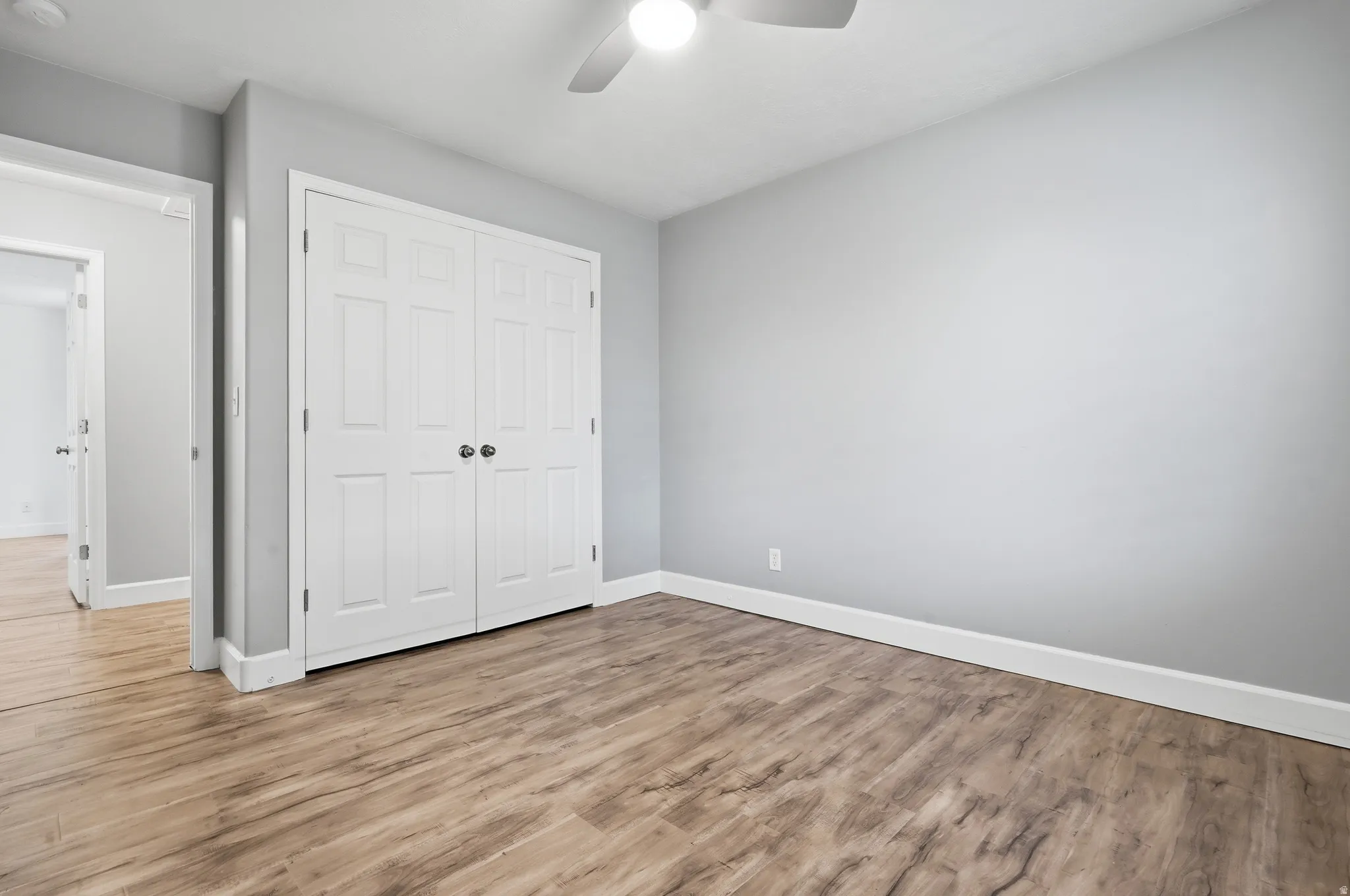 Wood-finish flooring, white panel bi-fold closet doors, ceiling fan with integrated lighting, and light gray wall paint