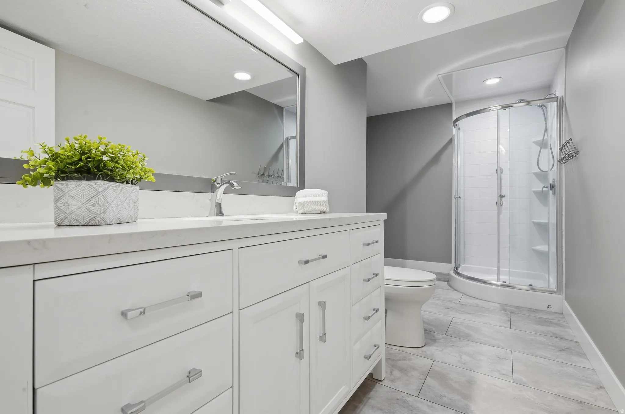 Bathroom featuring a curved glass shower enclosure, white vanity with ample storage, integrated sink, and a large wall-mounted mirror