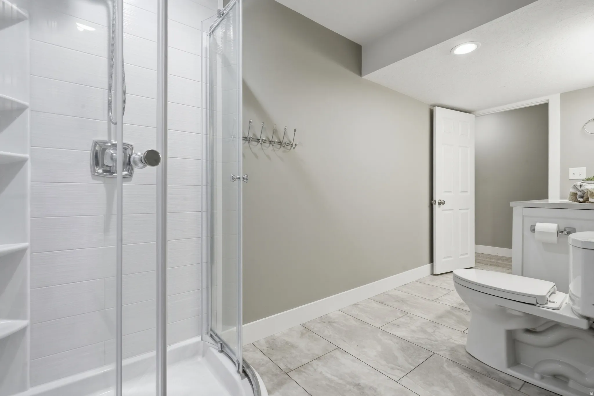 Modern primary bathroom featuring a frameless glass-enclosed shower with subway tile surround, dual vanity with white cabinetry and integrated sink, ceramic tile flooring, recessed lighting, and neutral wall finishes