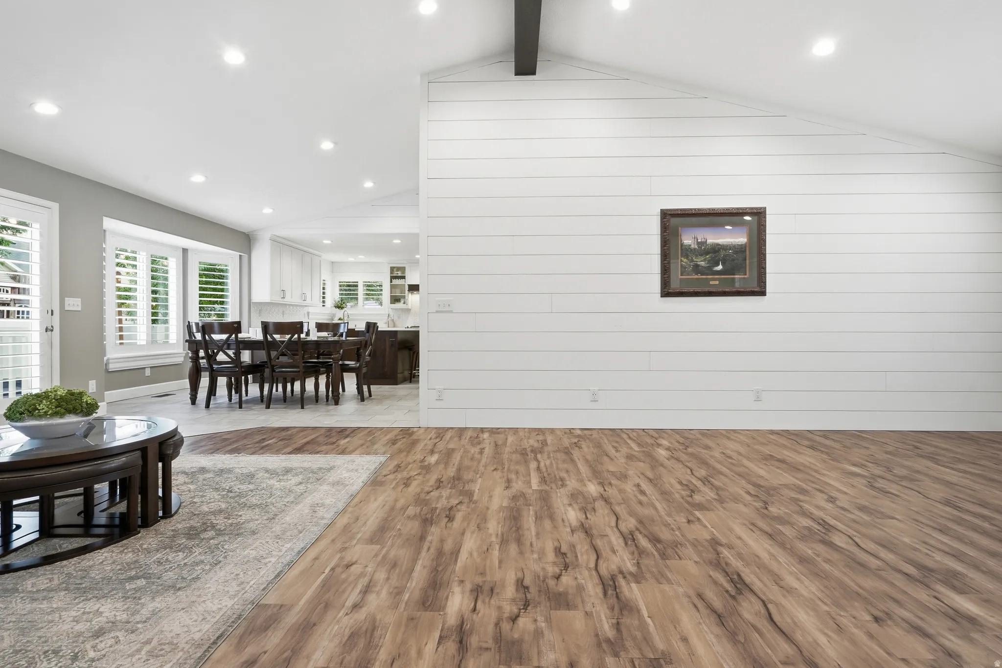 Spacious open-concept living area featuring vaulted ceilings with exposed beam detailing, recessed lighting, and white shiplap accent wall
