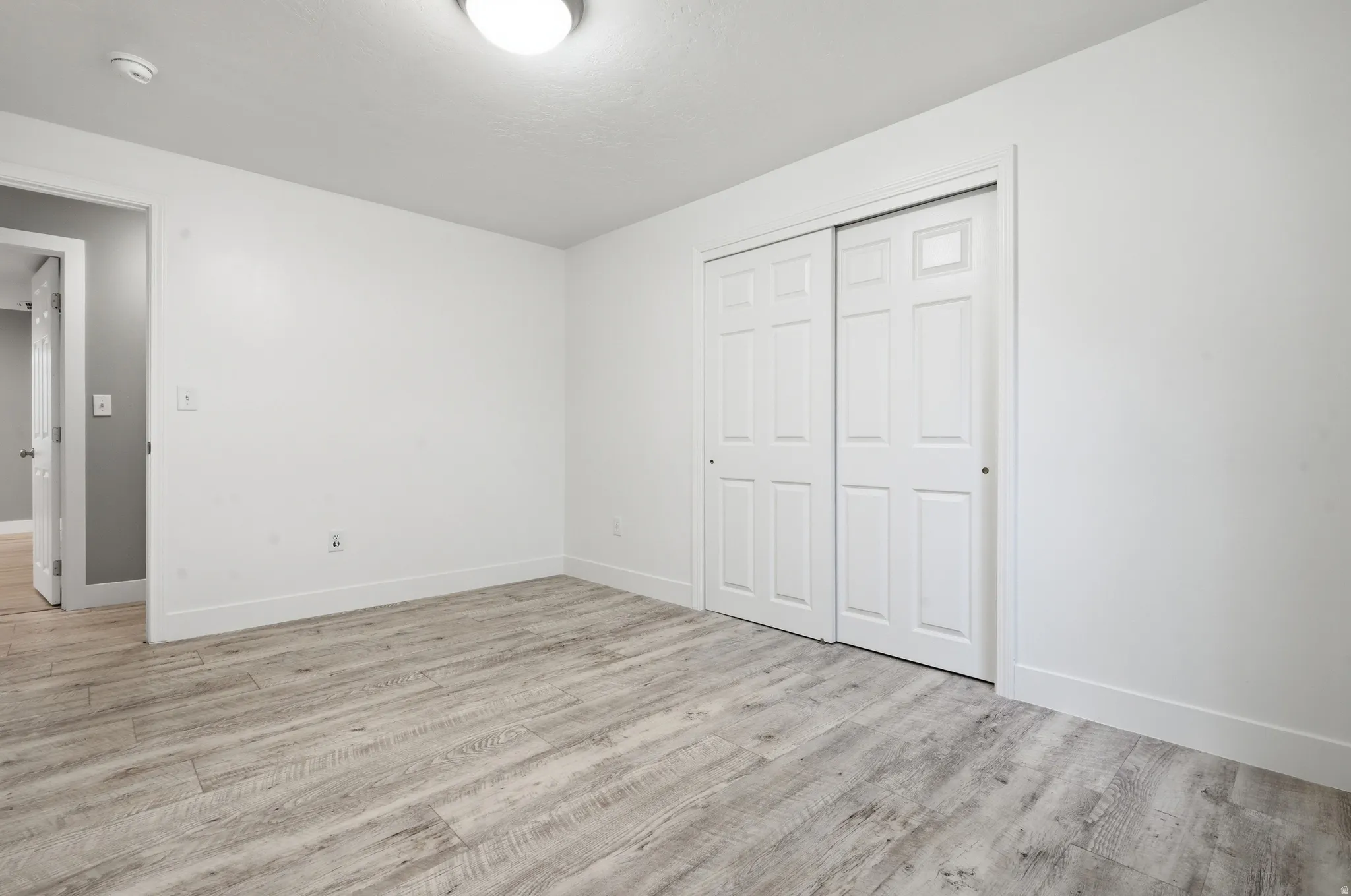 Neutral-toned wood-finish flooring, white walls, white trim, and a white bi-fold closet