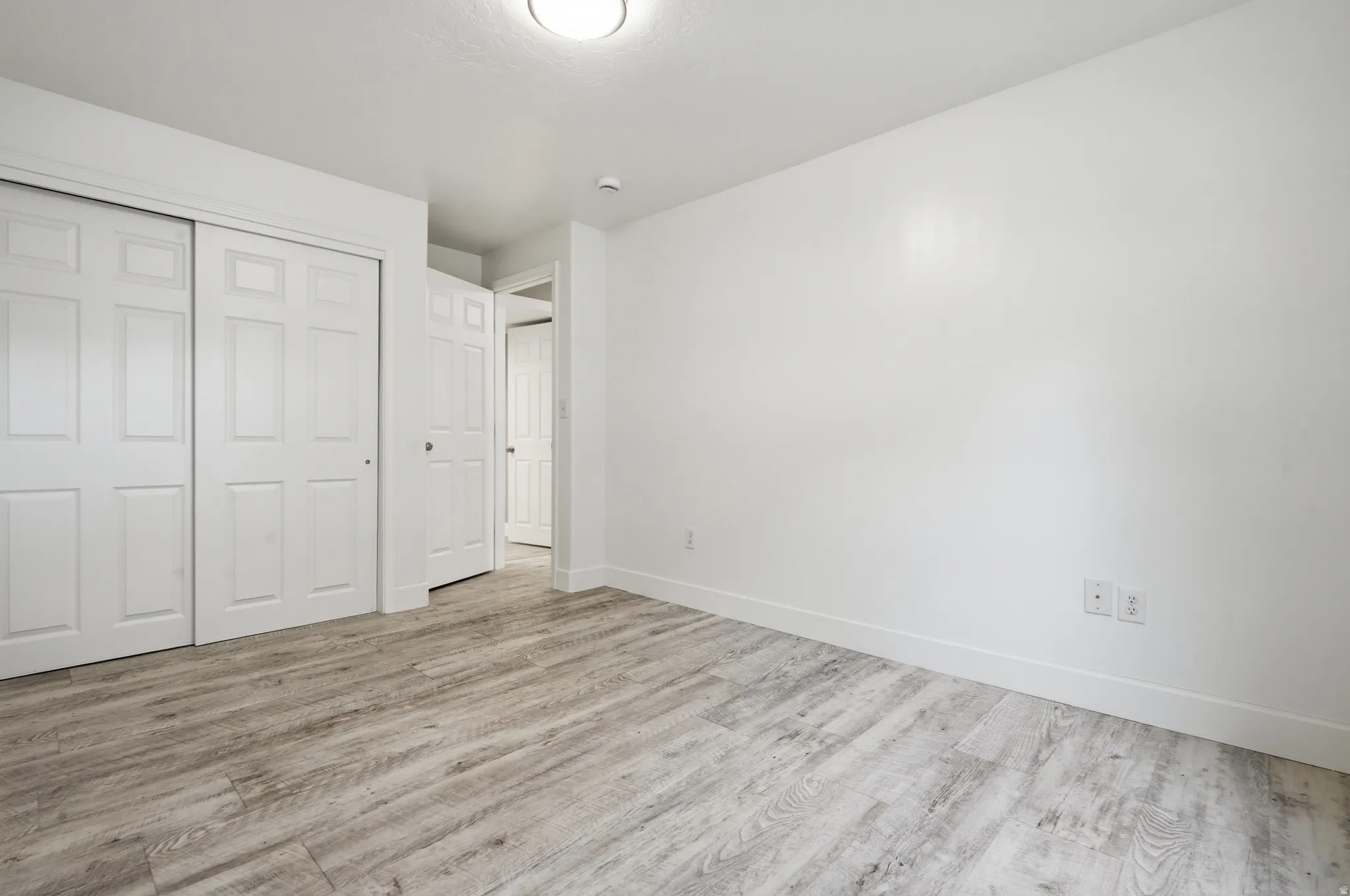 Spacious bedroom featuring wood-finish flooring, dual closets with six-panel doors, recessed ceiling lighting, and clean white walls with electrical outlets
